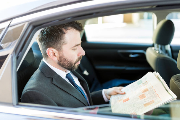 Przystojny połowy dorosłych biznesmen czytanie gazety siedząc w samochodzie - Zdjęcie, obraz