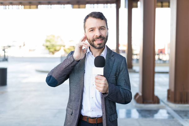 Portrait of mid adult TV reporter holding microphone while listening to earpiece at a broadcast - Photo, Image