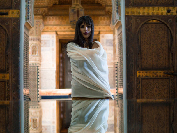 Menina marroquina bonita em vestido dourado curto e capa de manto branco em interior rico da pitoresca Dar Si disse Riyad em Marrakech
 - Foto, Imagem
