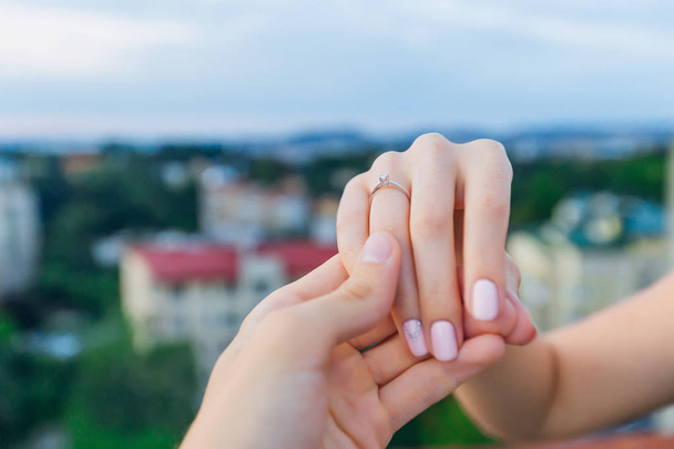 Adam kızın elini tutuyor ve yüzük parmağındaki yüzüğü gösteriyor. - Fotoğraf, Görsel