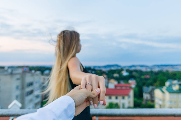 srác tartja a lány keze által, és gyűrű ábrázol a gyűrűs ujját, ő néz a város panorámája - Fotó, kép