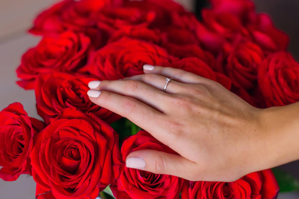 The guy holds a golden ring with a pebble on the background of red roses - Фото, изображение