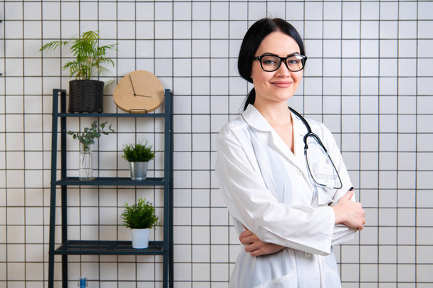 Mooie glimlachende dokter dragen inbg bril staan in haar moderne kantoor - Foto, afbeelding