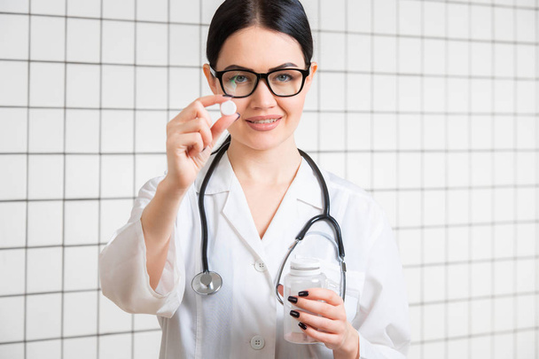 Выборочный фокус женщины-медсестры в белом халате показывает таблетки изолированы на медицинском фоне офиса
 - Фото, изображение