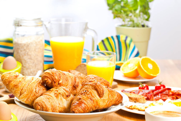 Крупный план свежих вкусных круассанов, апельсинового сока, мюсли и яиц с беконом на завтрак
 - Фото, изображение