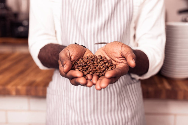 Nice professional barista holding roasted coffee beans - Foto, afbeelding