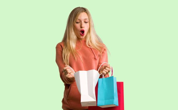 junges Mädchen überrascht mit vielen Einkaufstüten auf grünem Hintergrund - Foto, Bild
