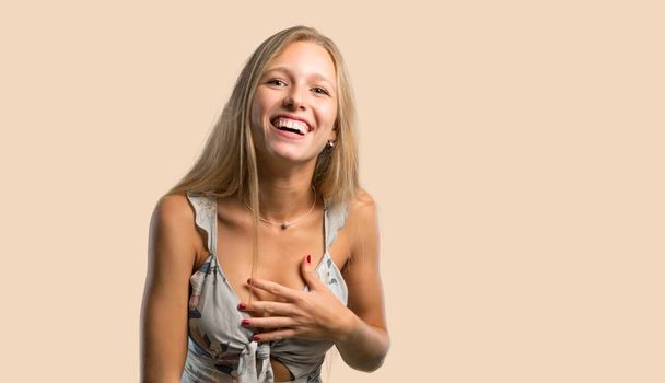 Young blonde woman smiling a lot while putting hands on chest on ocher background - Foto, imagen