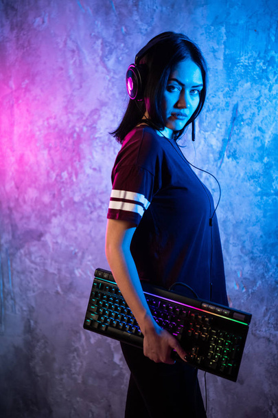 Mooie vriendelijke Pro Gamer Streamer meisje poseren met een toetsenbord in haar handen, het dragen van glazen. Aantrekkelijke Geek meisje met Cool Neon Retro kleuren in de achtergrond. - Foto, afbeelding