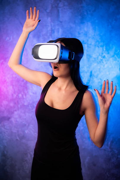 Wondering Young Woman in Virtual Reality Glasses over neon colored background. Shocked Girl wearing VR device. Close-up portrait of Female with VR headset. - Photo, Image