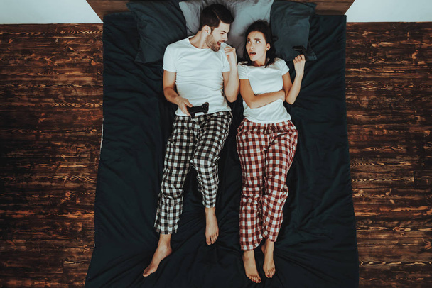 Couple is Lying on Bed. Couple is Young Beautiful Woman and Man. People After Playing Game on Joysticks. Man is Winning Woman and Celebrating. Girl is Upset. Persons in Home Interior. Top View. - Foto, Bild