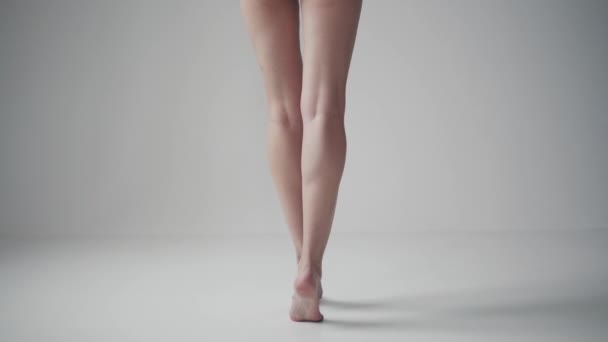jambes féminines se ferment. vue arrière. fille debout sur les orteils pieds nus sur un fond blanc
 - Séquence, vidéo