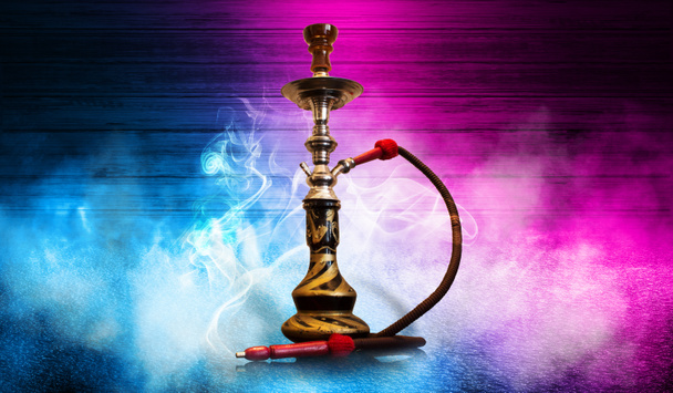 Smoking hookah on the background of an empty wooden wall and concrete floor. Spotlight light, blue and pink neon light, smoke - Photo, Image
