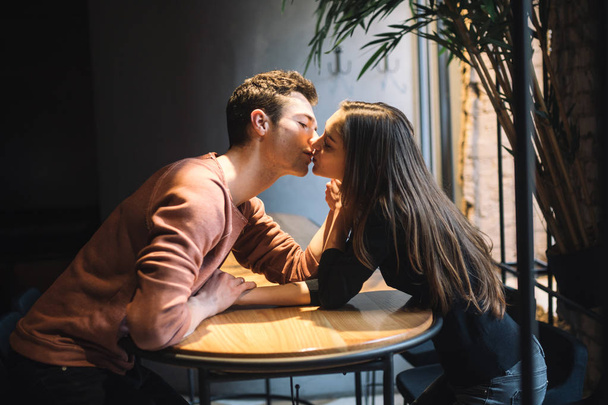 Theme love and holiday Valentines Day. couple of college students together in Caucasian heterosexual lovers winter inside the cafe sit at empty table embrace. Emotion happiness and love. - Photo, image