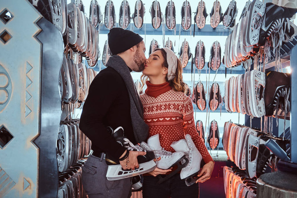 Young couple in love, kiss while standing near rack with many pairs of skates - 写真・画像