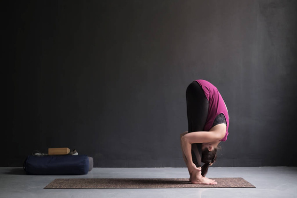 Mujer deportiva practicando yoga, de pie ejercicio de flexión hacia adelante, cabeza a rodillas, postura uttanasana. Longitud completa, vista lateral
 - Foto, imagen