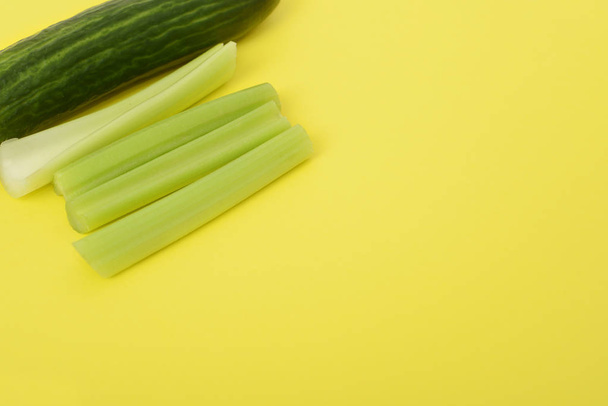 Celery stalks and cucumber in the corner isolated on yellow background. Space for text, copy space. Vegetarian background - Photo, Image
