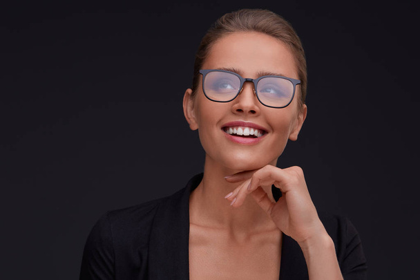 Elegant smiling woman in square eyeglasses on black background.Adult beautiful businesswoman in jacket.Black frame spectacles.Vision correction,optical shop,glasses store concept. - Photo, Image