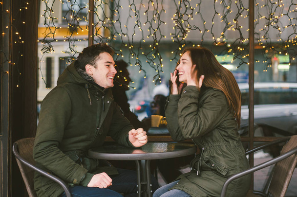 Theme love holiday Valentines Day. pair college students, Caucasian heterosexual lovers in winter, sit table of street cafe against the background window lights. Emotion romance of happiness and love. - Foto, Imagen