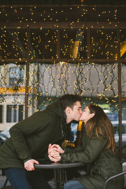 Theme love holiday Valentines Day. pair college students, Caucasian heterosexual lovers in winter, sit table of street cafe against the background window lights. Emotion romance of happiness and love. - Photo, Image