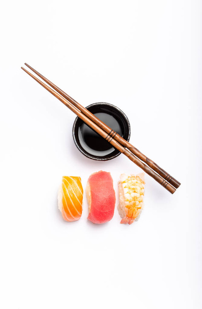 Set aus verschiedenen Sushi mit Lachs, Thunfisch und Garnelen, Sojasauce und Essstäbchen vor weißem Hintergrund, Draufsicht. traditionelles japanisches Sushi-Konzept, Nahaufnahme, flach la - Foto, Bild