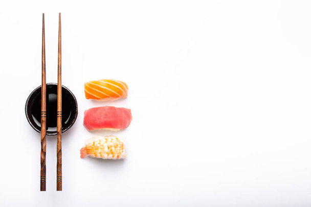 Set of different sushi nigiri, soy sauce and chopsticks over white background with copy space, top view. Traditional Japanese sushi concept, close-up - Foto, afbeelding