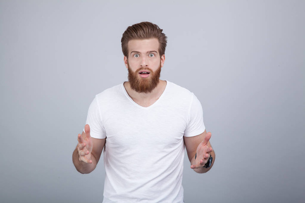 Amazed bearded man dressed in a white T-shirt looking into the camera with wide-open eyes - Photo, Image