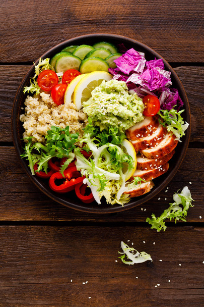 Buddha bowl dish. Healthy balanced lunch with quinoa, grilled chicken meat, lettuce salad, pepper, cucumber, tomato and avocado guacamole with lemon - Fotó, kép