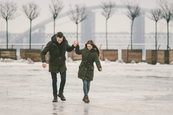 theme bad weather in winter, thawing in spring, poor snow removal work for urban utilities. Danger of injury falling, slipping on ice and getting injured. Caucasian couple laugh joy slide on square. - 写真・画像