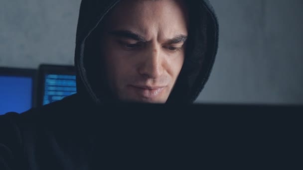 Mannelijke hacker in kap werken op een computer in een donkere kantoorruimte. Geschoten op steadicam - Video