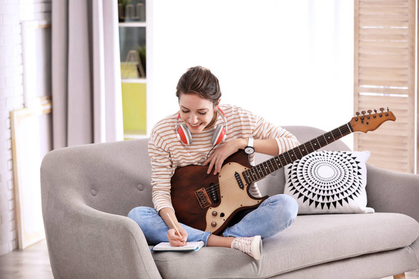 Young woman with electric guitar composing song in living room - Zdjęcie, obraz