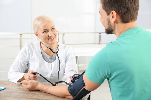 Lääkäri tarkistaa kypsän naisen pulssin lääketieteellisellä laitteella sairaalassa, lähikuva
 - Valokuva, kuva