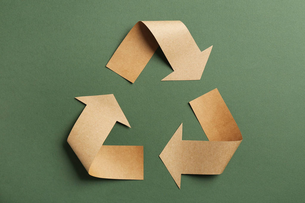 Recycling symbol cut out of kraft paper on green background, top view - Фото, изображение