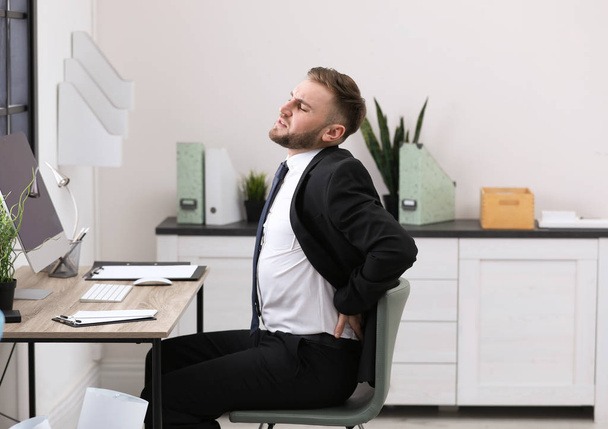 Businessman suffering from back pain at workplace - Foto, imagen