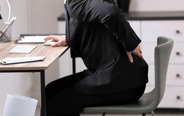 Businessman suffering from back pain at workplace, closeup - Fotó, kép