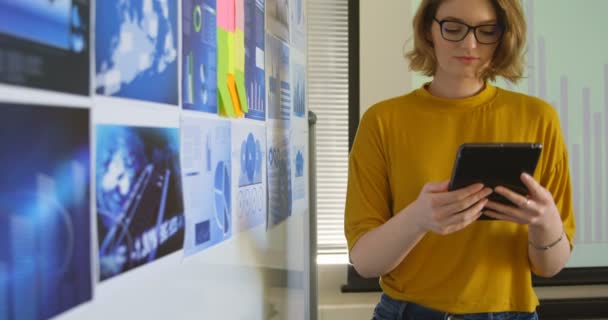 Front view of young caucasian businesswoman looking at graphs in modern office. Young caucasian businesswoman holding digital tablet in office 4k - Filmagem, Vídeo