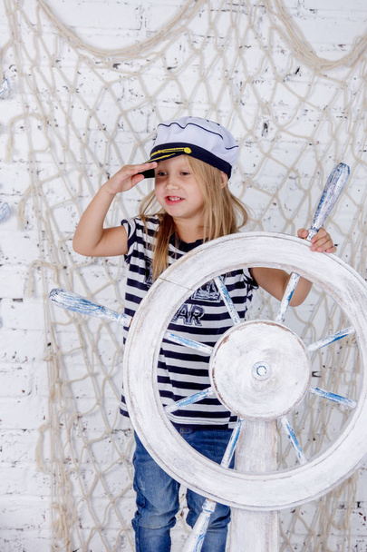 Portrait of one cute and mischievous european girl in a sea style studio on a white brick wall background - Photo, Image