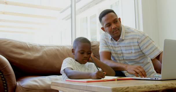 Front view of black father helping his son with homework at home. Black father using laptop at home 4k - Materiaali, video