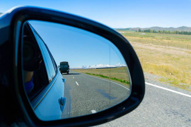 В зеркале заднего вида пейзаж и тяжелый грузовик на дороге сзади
. - Фото, изображение