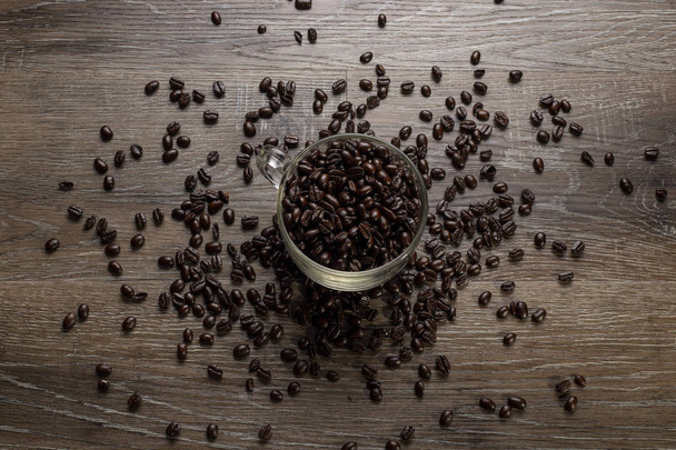 Cup of dark roasted coffee beans arranged on a wooden table for copyspace or text - Fotoğraf, Görsel