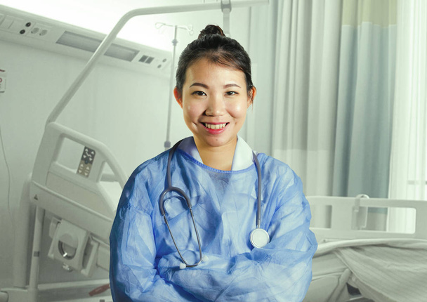 young happy and attractive Asian Chinese medicine doctor woman in blue scrubs smiling cheerful at hospital room bed in health care and successful medical career concept - Foto, afbeelding