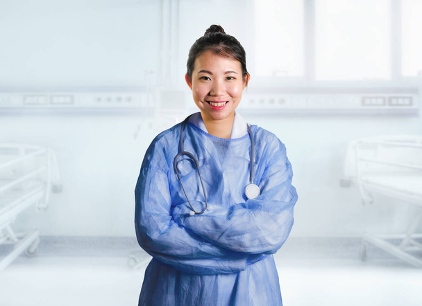 young happy and attractive Asian Korean medicine doctor woman in blue scrubs smiling cheerful at hospital room bed in health care and successful medical career concept - Foto, Bild