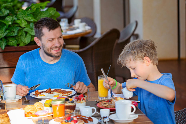 ευτυχισμένη οικογένεια των δύο, πατέρας και γιος, απολαμβάνοντας νόστιμο πρωινό που όλοι μαζί στις διακοπές ή στο σπίτι - Φωτογραφία, εικόνα