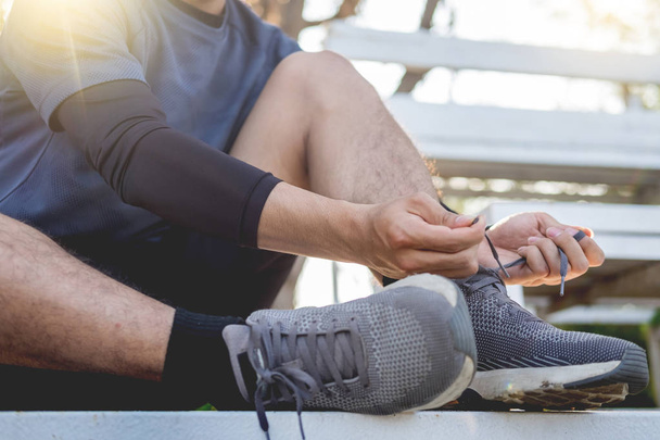Чоловік-спортсмен зав'язує взуття мереживами в мінімалістичних кросівок з босоніжками, готуючись до тренувань. Спортивні тренування та концепція здорового способу життя
. - Фото, зображення