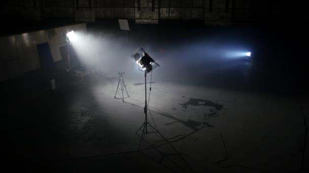 dunkles Fotostudio mit hellen Scheinwerfern. geräumiger dunkler Raum mit mitgeliefertem Flutlicht und Kamera auf Stativ für professionelle Aufnahmen - Filmmaterial, Video