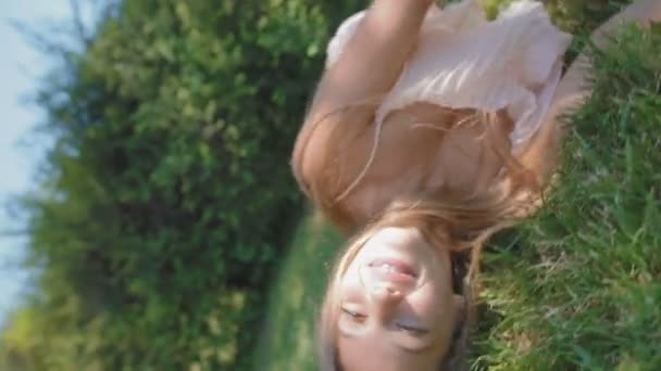 young woman rolls on lush grass laughing and camera turns up-side-down in park - Footage, Video