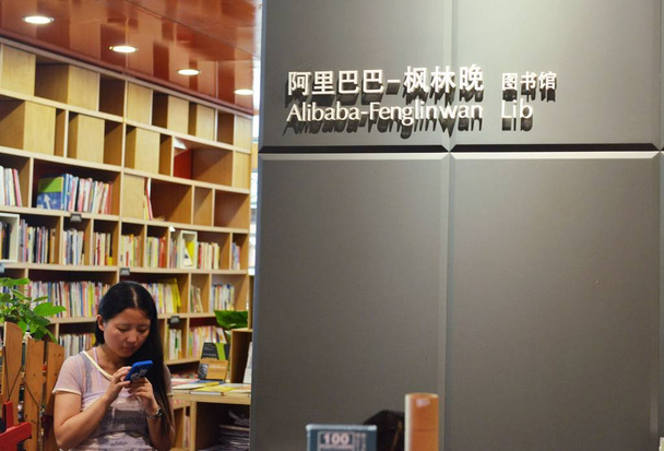 A Chinese employee uses her mobile phone in the Alibaba Fenglinwan Library at the headquarters of Chinese e-commerce giant Alibaba Group in Hangzhou city, east Chinas Zhejiang province, 19 September 2014 - Фото, зображення