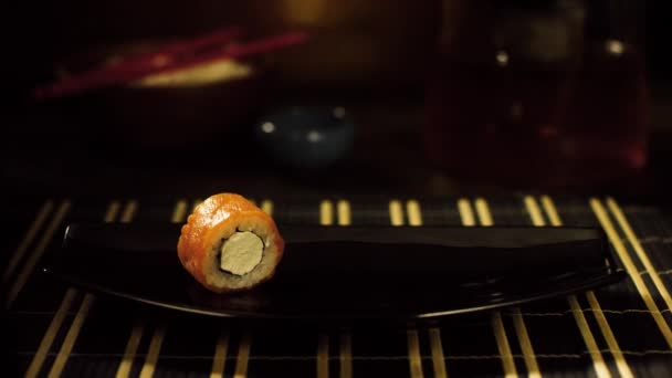 Detail sushi rolka na desce. Osamělý sushi rolka s lososem a sýrem je na černé desce, která má ruku v černé rukavici - Záběry, video