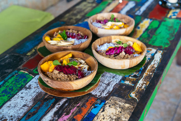Close up four smoothies bowls made with mango, banana, granola, grated coconut, dragon fruit, chia seeds and mint on colored background - 写真・画像