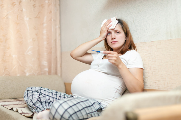 pregnant woman with thermometer in living room - Valokuva, kuva